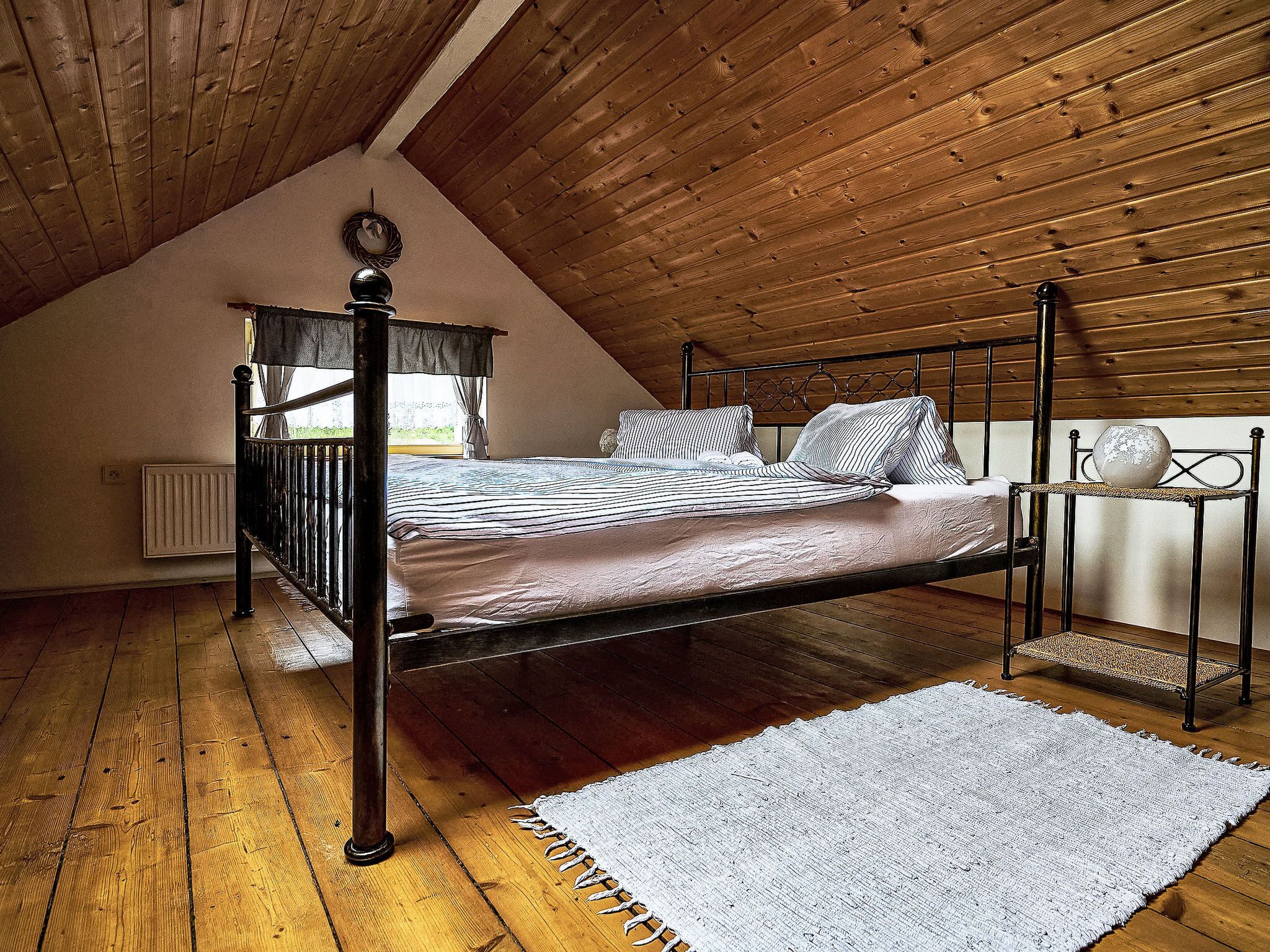A bedroom with a four-poster bed, a white radiator, wooden flooring, and a sloped ceiling.