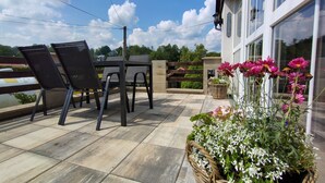 An outdoor patio with a table and chairs, a wicker basket with flowers, and a view of a building with large windows. - U sjezdovky by Interhome (Smržovka)
