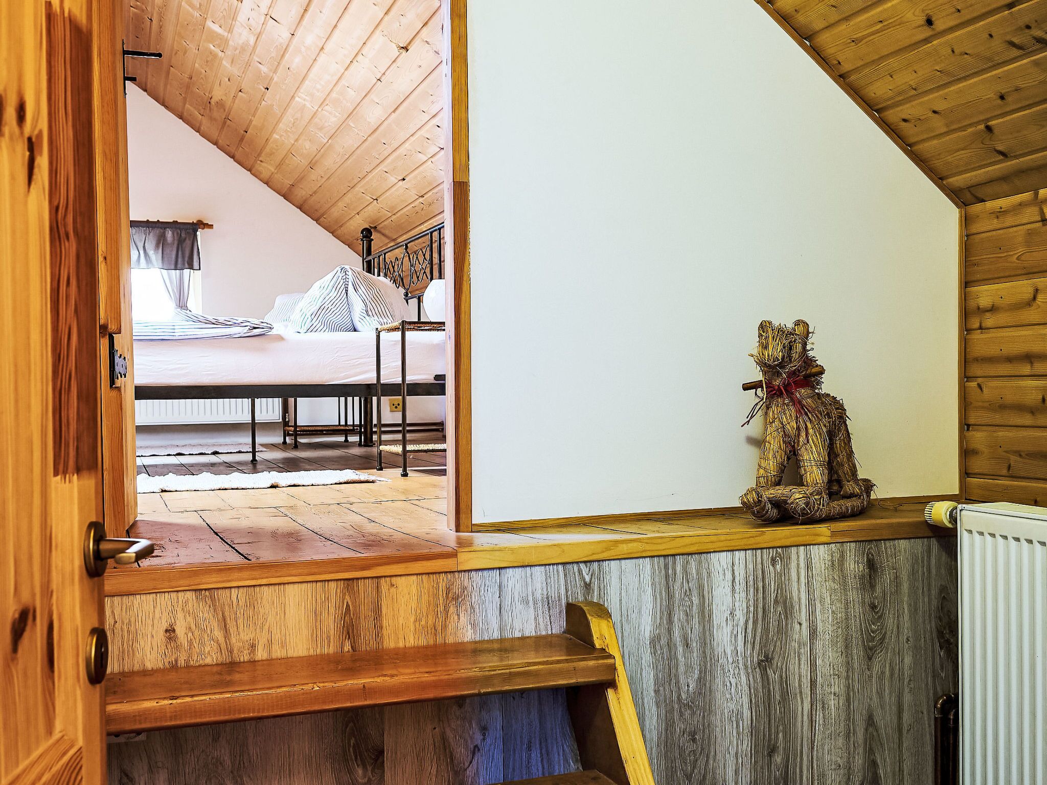 A wooden staircase leading to a bedroom with a bed and a decorative bear statue.