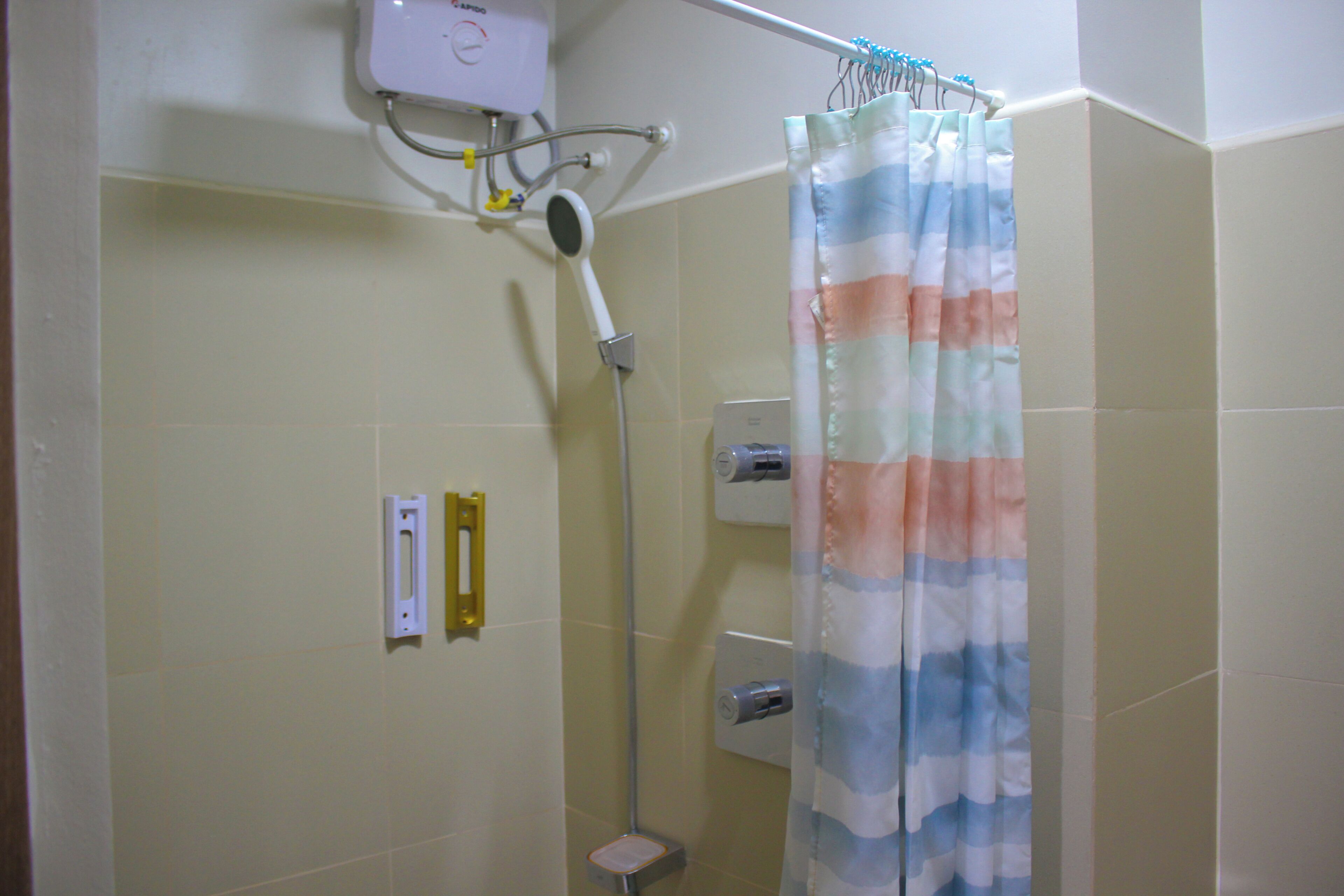 A shower with a striped curtain, a handheld showerhead, and a wall-mounted control panel.