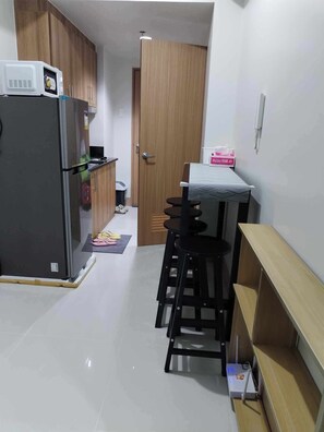 Compact kitchen with a refrigerator, microwave, and dining area featuring a table and stools.