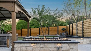 A stone fire feature with a wooden pergola overhead, surrounded by a wooden fence and trees. - Arvada Olde Town Oasis Accomodates 24 People (Arvada)