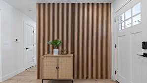 A hallway with a wooden slatted wall, a wicker cabinet with a plant, and white doors. - Arvada Olde Town Oasis Accomodates 24 People (Arvada)