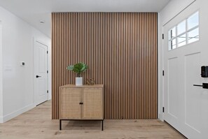 Um corredor com parede de ripas de madeira, um armário de vime com uma planta e portas brancas.