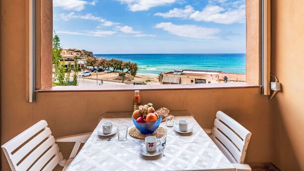 A balcony with a table set for two, overlooking a coastal view with buildings and a clear sky. - Bella Vista by Interhome (Algajola)