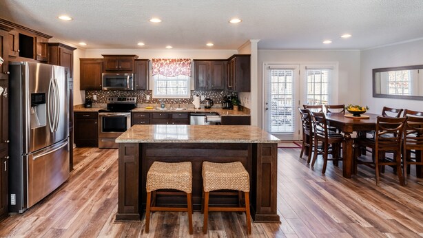 Una cocina con una isla central, armarios de madera, electrodomésticos de acero inoxidable y una zona de comedor con sillas de madera.