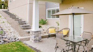 Un patio cubierto con una mesa, sillas, una escalera y un pequeño jardín.