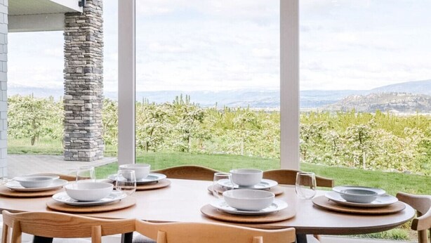 Un comedor con una mesa dispuesta para seis personas, ventanas amplias que ofrecen vistas a un viñedo y montañas distantes.