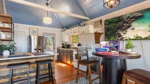 A kitchen with wooden bar stools, a dining table, and a painting of a beach scene.
