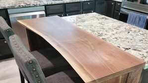 A kitchen with a wooden island, dark cabinetry, and a marble countertop.