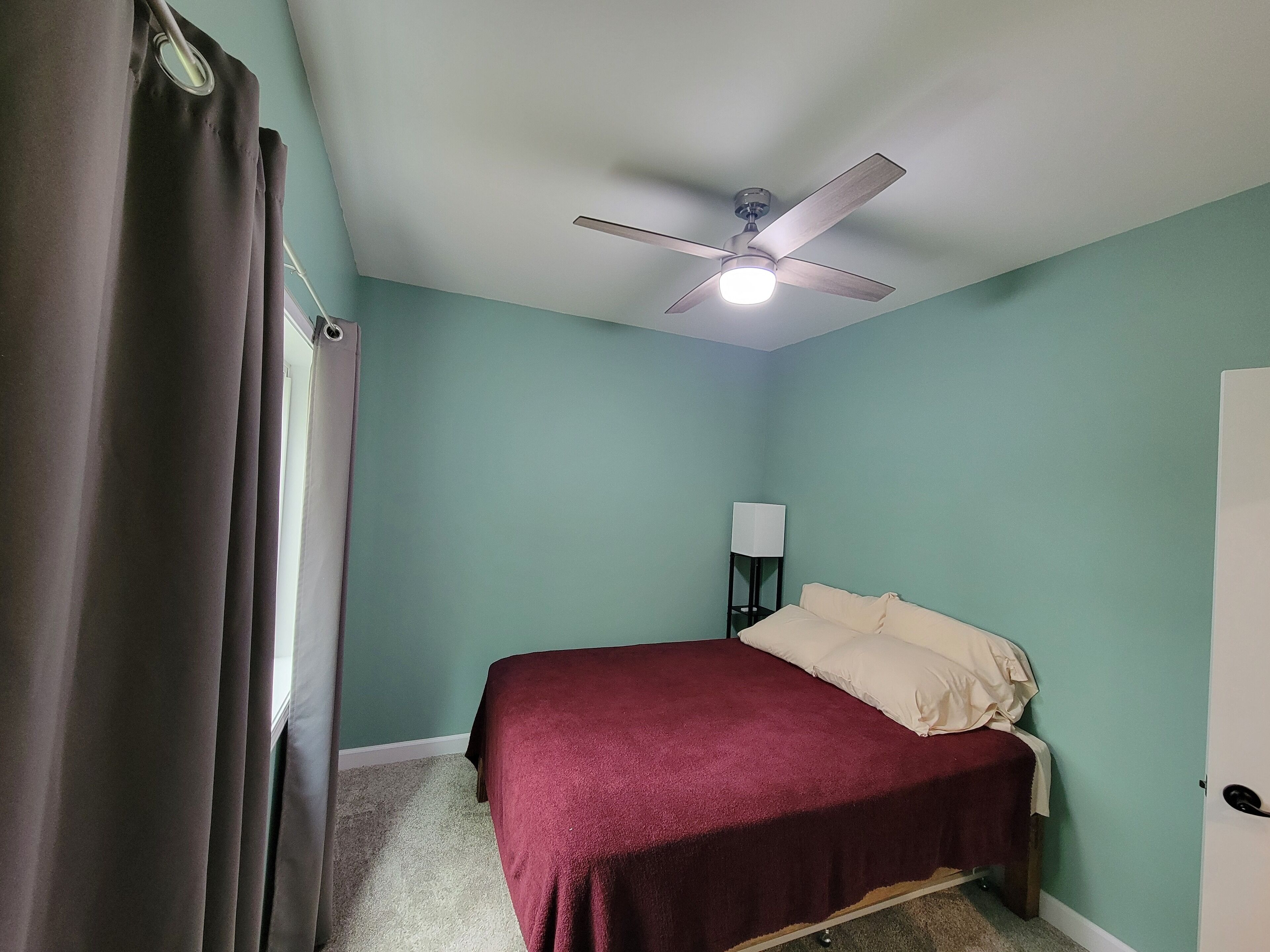 Une chambre à coucher avec un lit, un ventilateur de plafond, une table de chevet et une porte.