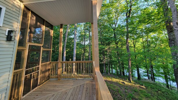 A wooden deck with a covered porch, large windows, and a view of a forested area.