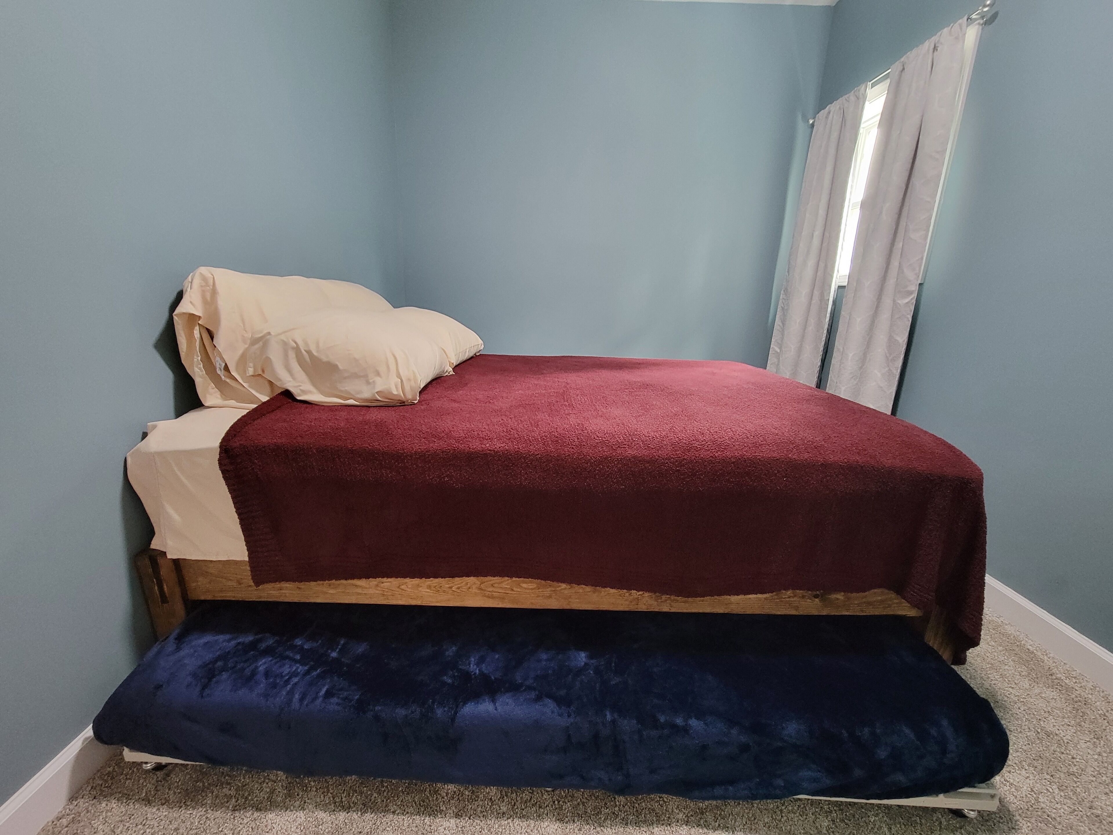 A bedroom with a bed, a window with curtains, and a carpeted floor.