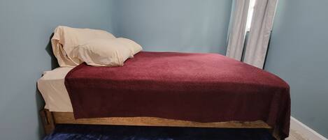A bedroom with a bed, a window with curtains, and a carpeted floor.