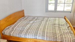 Una cama individual con una colcha estampada en una habitación con suelo de madera y ventana con vistas a árboles.