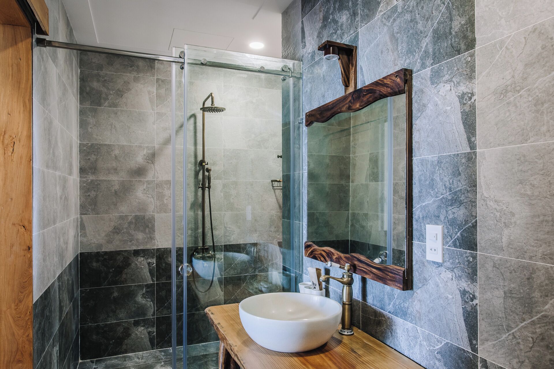 A modern bathroom with a glass-enclosed shower, a wooden vanity, and a large mirror.
