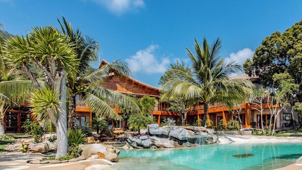 Un resort con piscina, palmeras y un edificio con techo de paja.