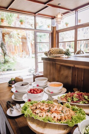 A dining area with a wooden table set with various dishes, including shrimp and salad, and a view of the outdoors through large windows. - Rocks Beach Boutique Phu Quoc (Phu Quoc)