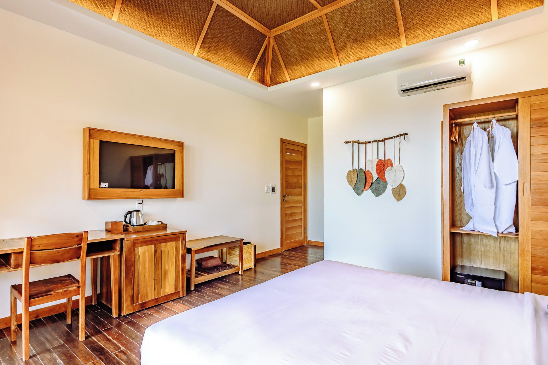 Habitación de hotel con un escritorio de madera, una cama, un armario, un espejo y un aire acondicionado instalado en la pared.