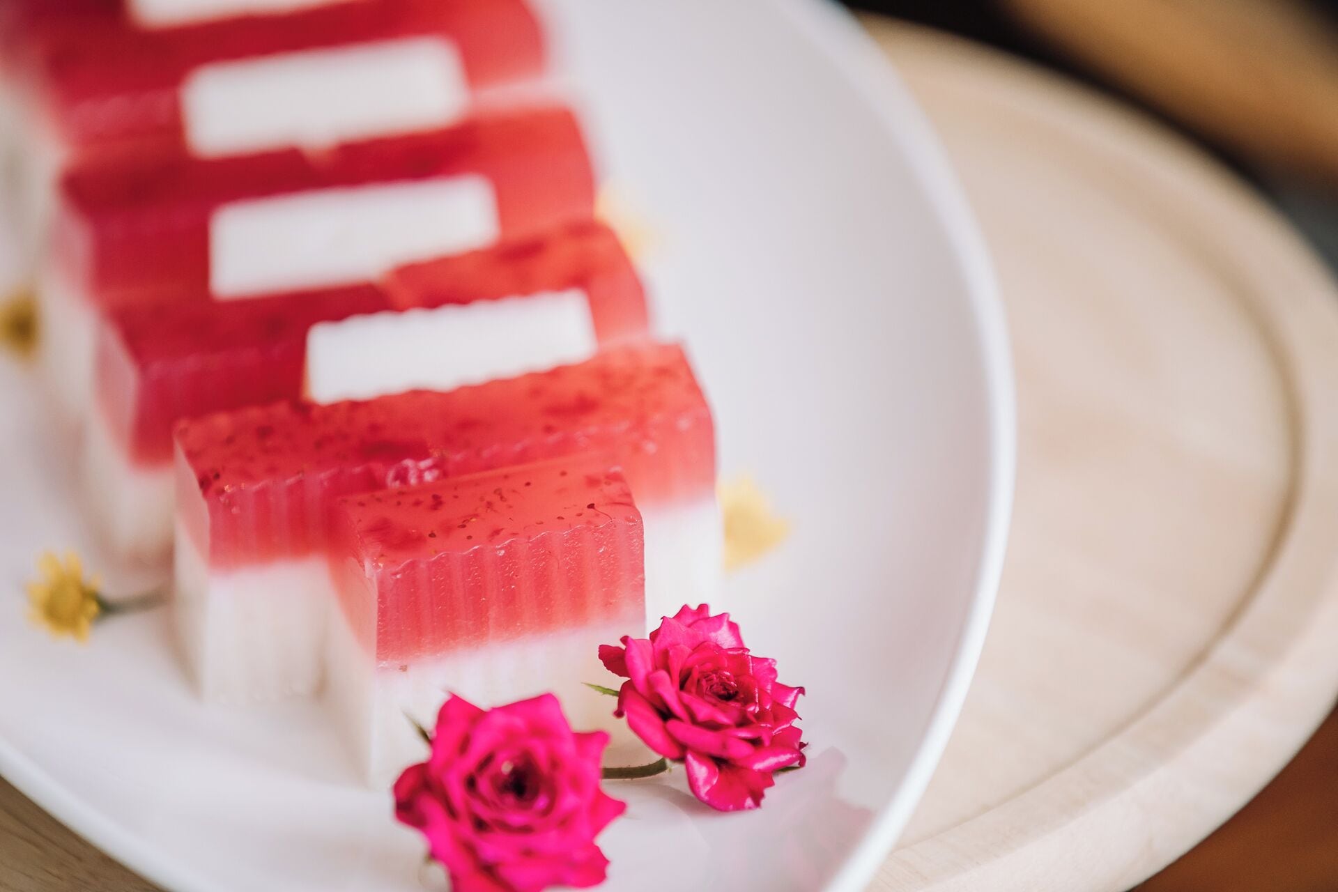 A dessert on a white plate with pink and white layers, accompanied by pink roses.