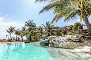 A clear turquoise pool surrounded by palm trees and rocky formations, with a thatched-roof building in the background. - Rocks Beach Boutique Phu Quoc (Phu Quoc)