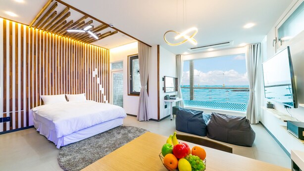 Una habitación de hotel moderna con cama, una mesa de comedor con fruta, televisor y vista al mar.