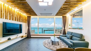 Una sala de estar moderna con un televisor grande, un sofá, una mesa de centro y vista al mar con aerogeneradores.
