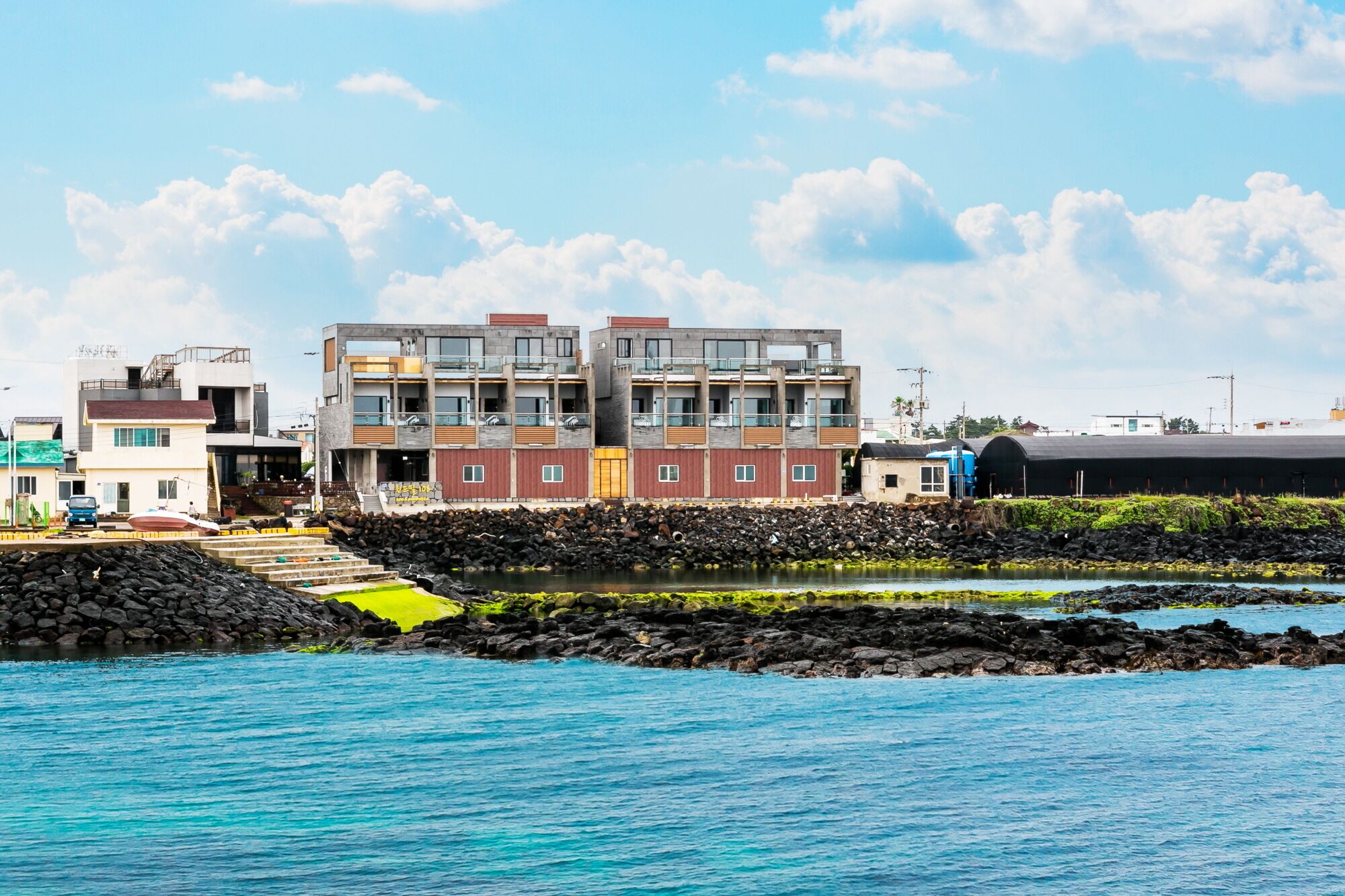 A coastal building with multiple floors, a rocky shoreline, and a clear blue sky.