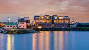 Un edificio frente al agua con varios balcones y ventanas grandes que reflejan el atardecer.