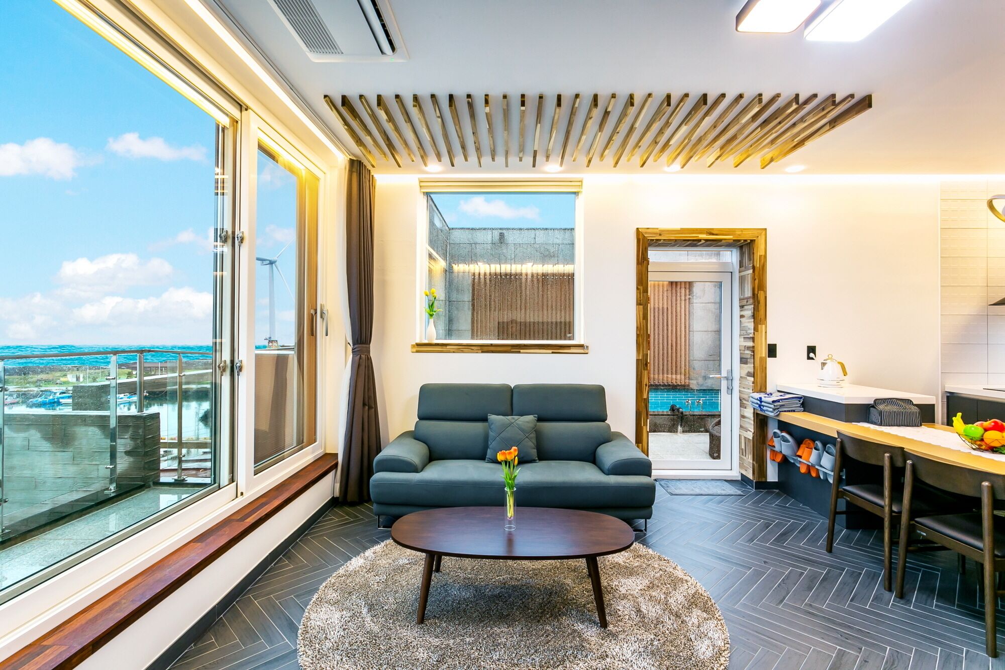 Un salón moderno con un sofá, una mesa de centro y vistas de la ciudad a través de grandes ventanales.