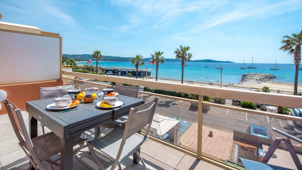Een balkon met een tafel gedekt voor twee, met uitzicht op een strand met boten en palmbomen.