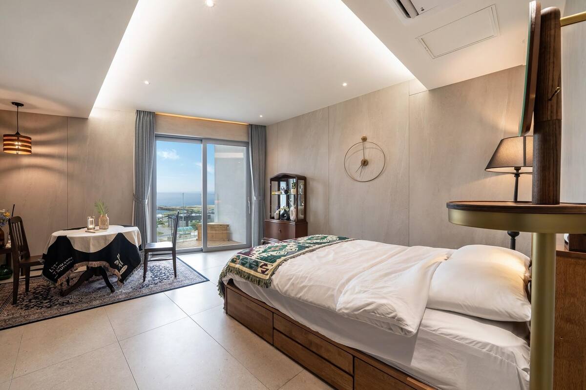 Ein modernes Schlafzimmer mit einem großen Bett, einem Schreibtisch und Blick auf das Meer.