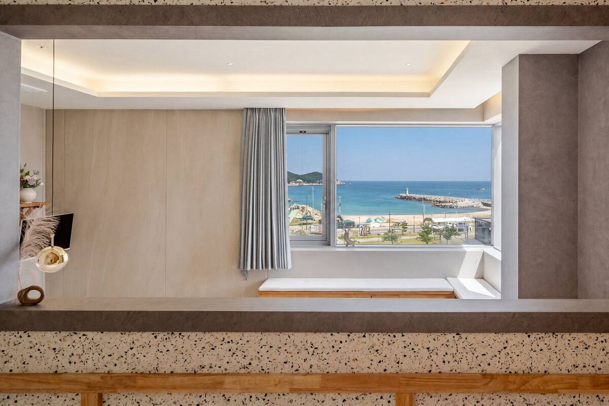 Ein modernes Zimmer mit großem Fenster, einer Bank und Blick auf den Strand.