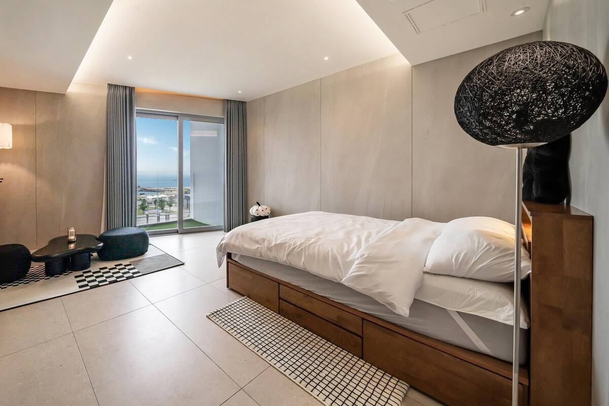 Ein modernes Hotelzimmer mit einem großen Bett, einem Schreibtisch, einem Stuhl, einer Lampe und Blick auf die Stadt.