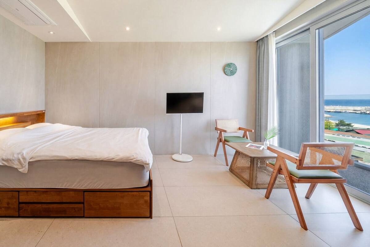 Ein modernes Hotelzimmer mit einem Holzbett, einem Flachbildfernseher, einem kleinen Tisch und einem Sessel.