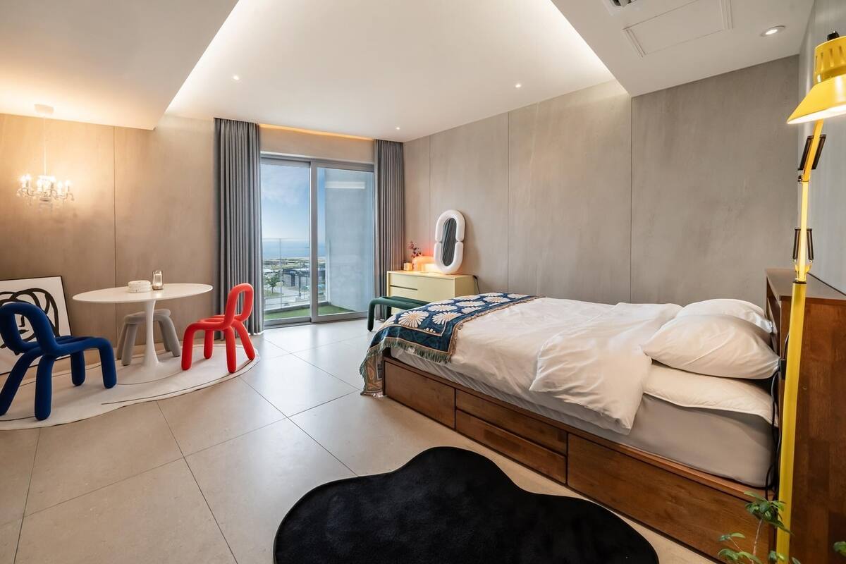 Ein modernes Hotelzimmer mit Bett, Schreibtisch, Stuhl und Blick ins Freie.