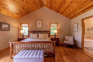 A bedroom with a wooden ceiling, a large bed with a headboard, two bedside tables with lamps, a chair, and a view of a bathroom. - 5 O'Clock between Boone & Blowing Rock - Views, hot tub, BBQ smoker, pool table!  Minutes to town. (Blowing Rock)