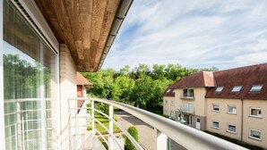 Un balcon donnant sur un quartier résidentiel, avec notamment un immeuble doté de nombreuses fenêtres et une voiture garée.