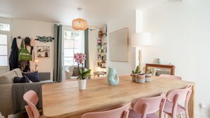 A modern living room with a wooden dining table, pink chairs, a white sofa, and a large window with curtains. - La Trouvillaise by Interhome (Deauville-Trouville)