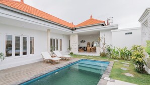Een modern huis met zwembad, een witte gevel en een terras.