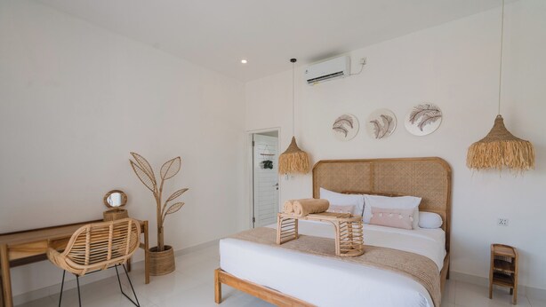 Een slaapkamer met een houten bed, een rieten stoel, een klein tafeltje en decoratieve wandkunst.