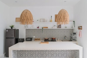 A modern kitchen with a central island, two hanging light fixtures, a patterned backsplash, and a built-in refrigerator. - Noel Peaceful 3BR Villa (Munggu)
