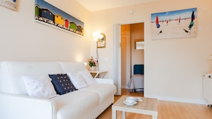 A modern living room with a white sofa, a small wooden coffee table, and a painting of colorful beach huts on the wall. - Apartment Ascot by Interhome (Deauville-Trouville)