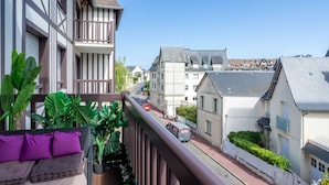 A balcony with a view of a street, potted plants, and a building with a sloped roof. - Apartment Ascot by Interhome (Deauville-Trouville)