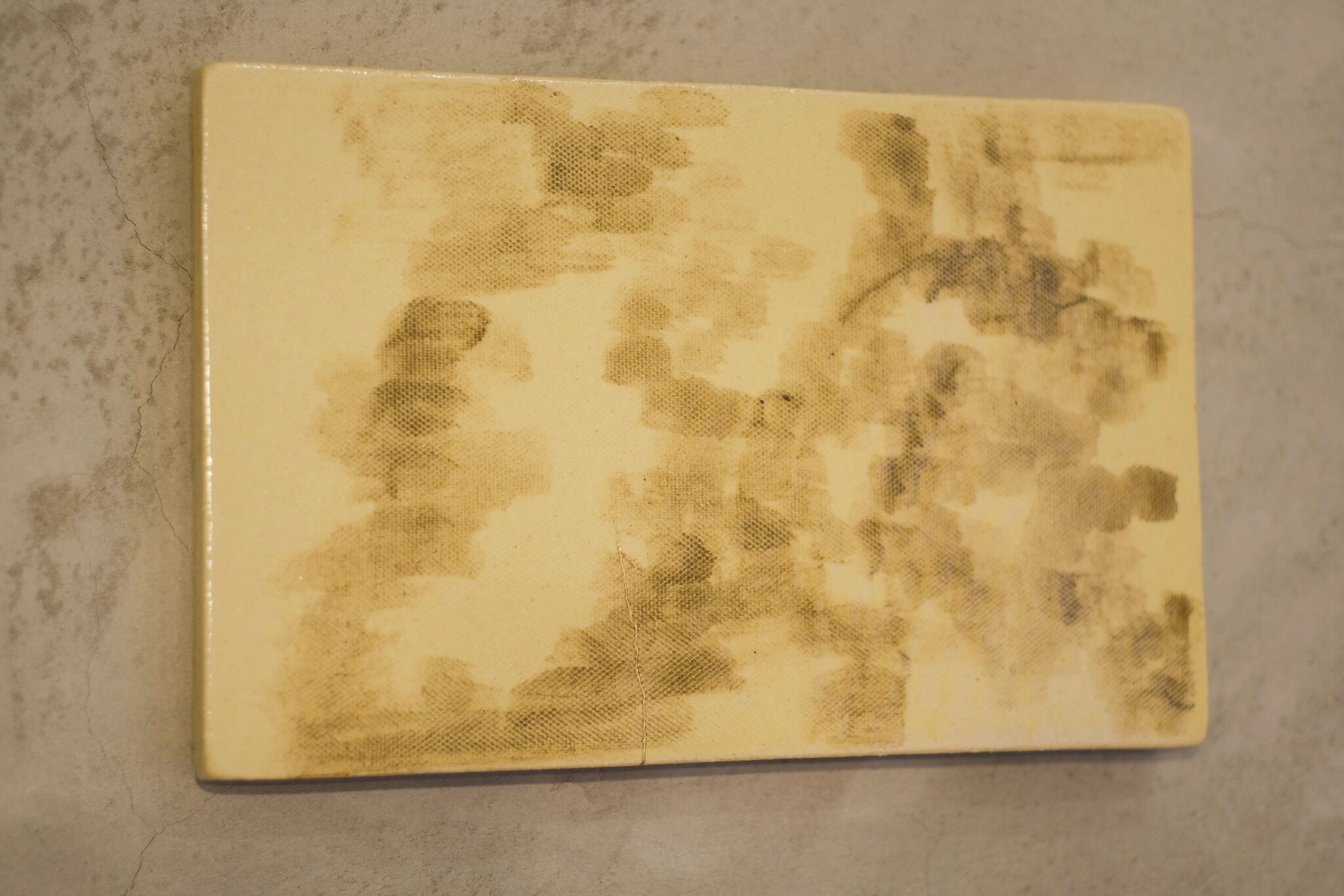 A rectangular object with a yellowish surface and brownish stains.