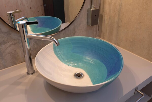 Un baño con un lavamanos blanco y un lavabo azul, un grifo cromado y un espejo sobre el lavamanos.