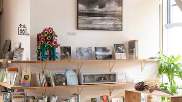 A room with a bookshelf filled with books and decorative items, a framed photograph on the wall, and a window with a view of the outdoors.