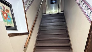 Un escalier en bois avec une rampe, un paillasson au bas et une œuvre d’art florale encadrée accrochée au mur.