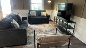 A living room with two sofas, a TV on a stand, and a window with a view.
