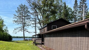 A wooden cabin with a deck, surrounded by a well-maintained lawn and a stone pathway leading to the water.